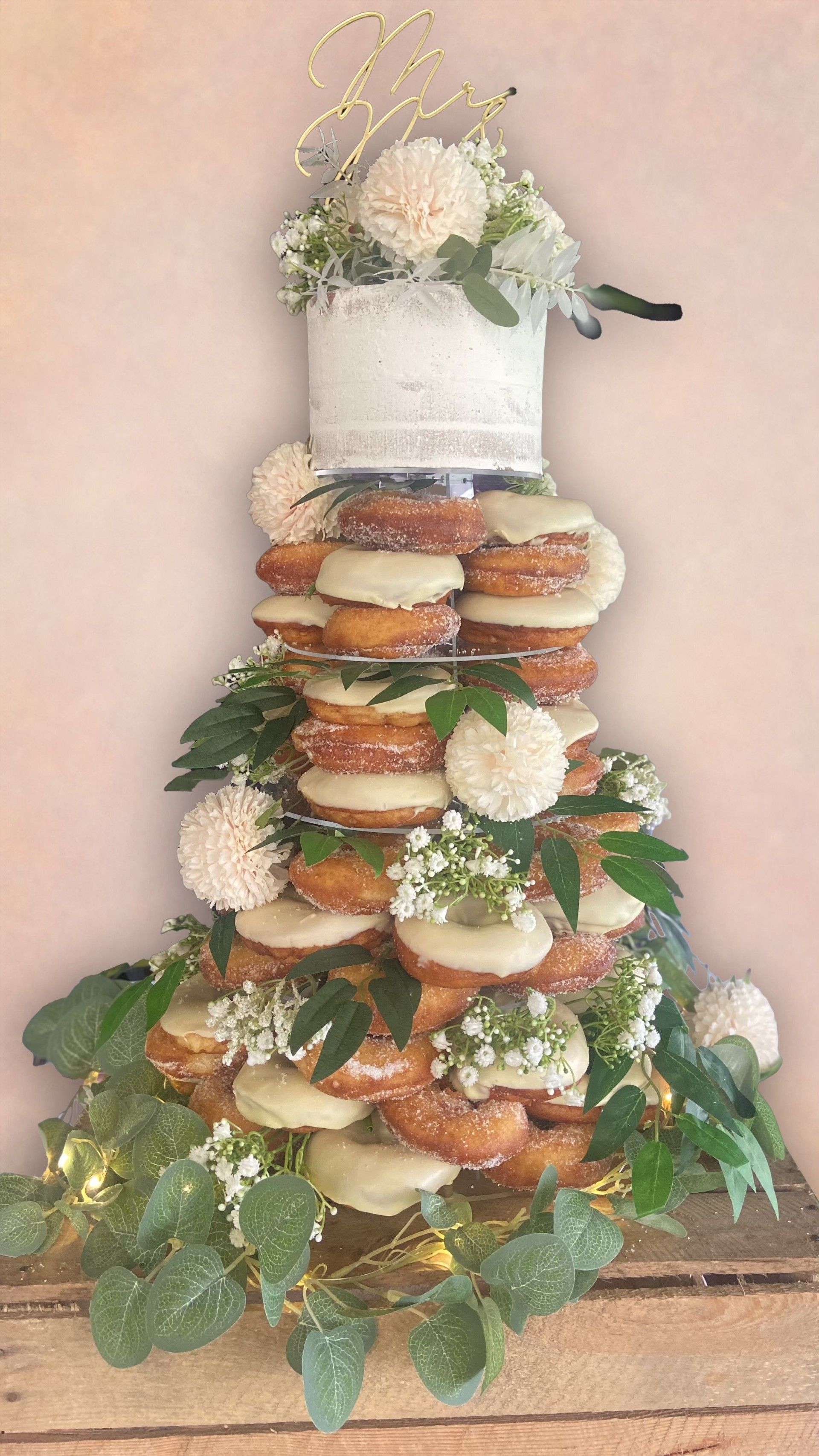Donut tower with small top cake, decorated with white flowers and greenery.