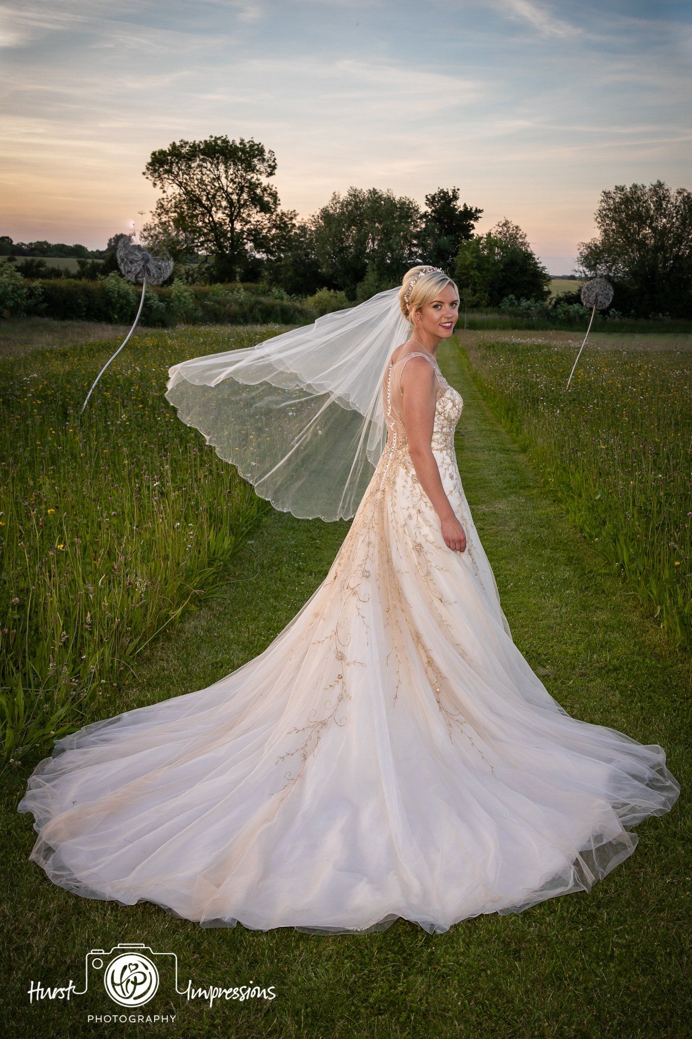 Bride in a white gown and veil standing in a field at sunset.