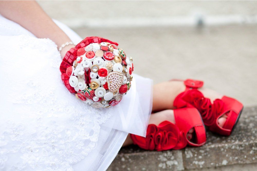 Bride in white dress with red button bouquet and matching red platform heels.