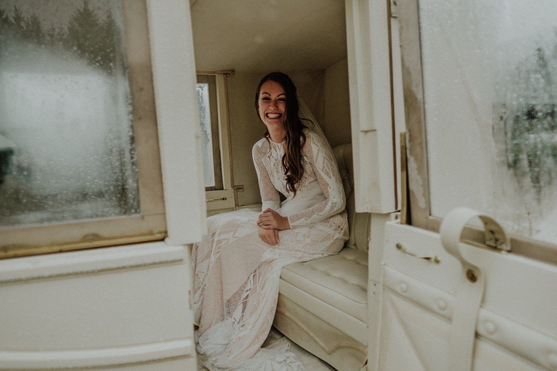 Bride in white dress smiles while seated inside white carriage.