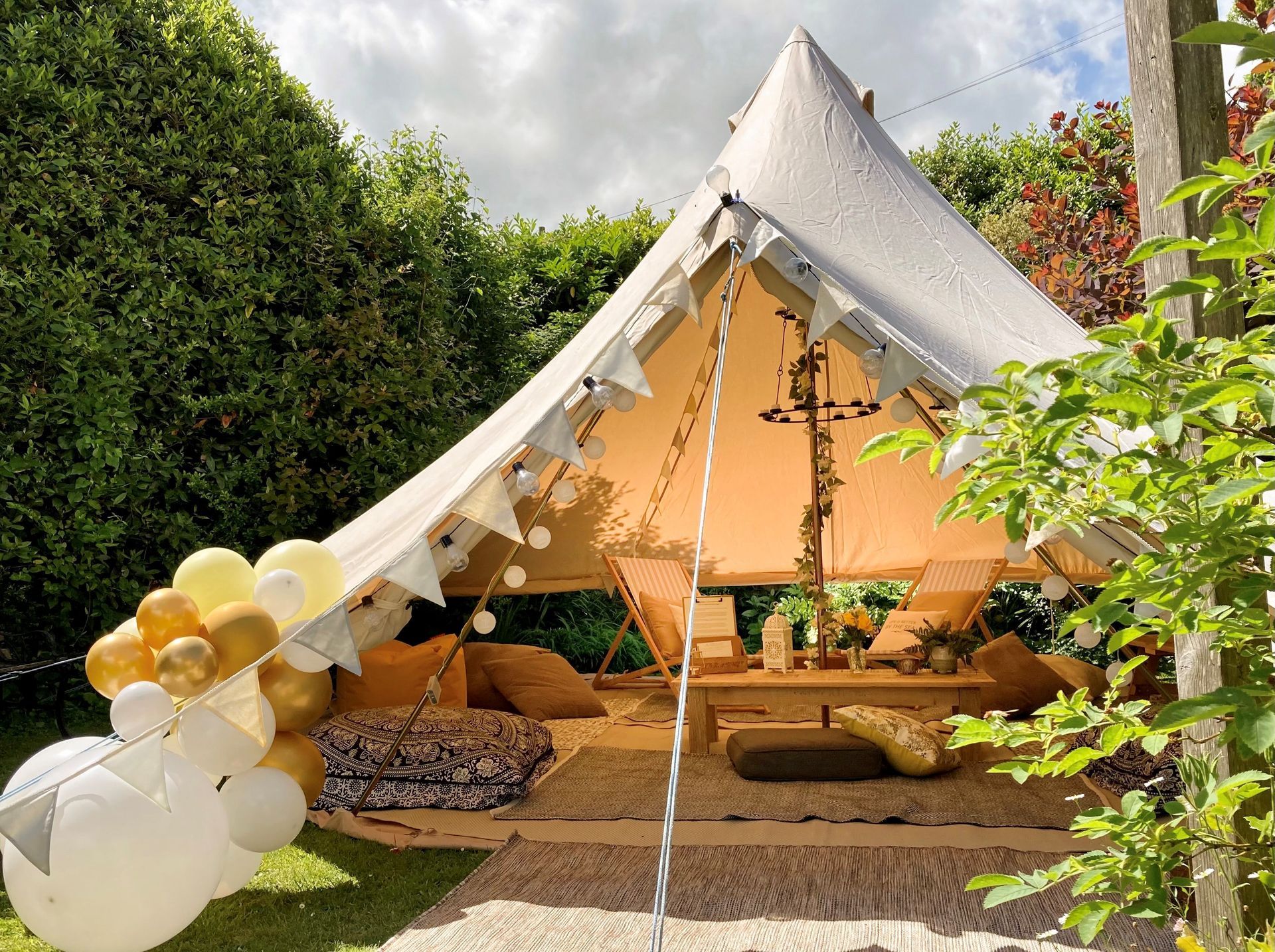 Bell tent decorated for a party, set in a garden with balloons.