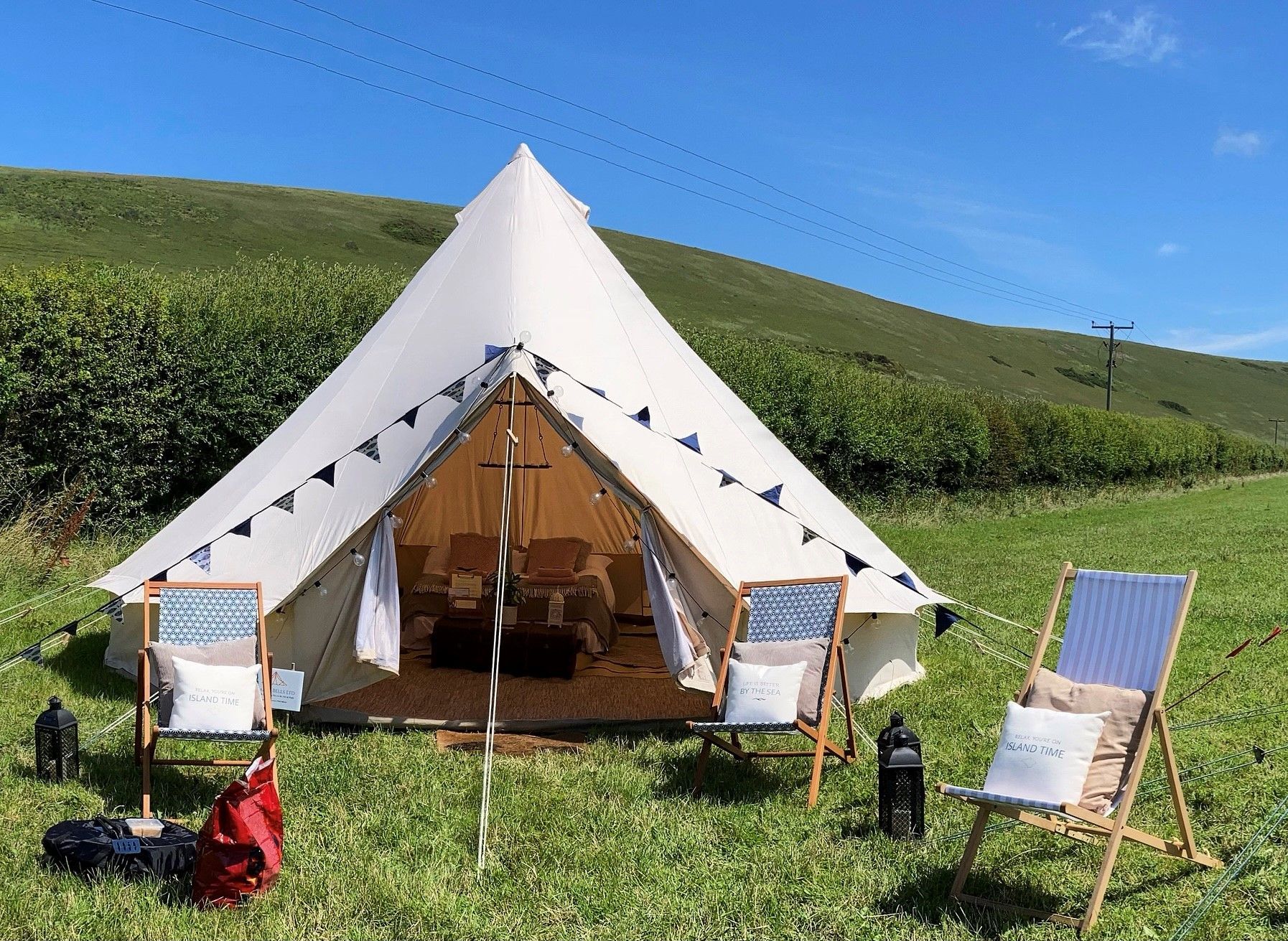 Beige bell tent in a grassy field with chairs, decorations, and a green hill.