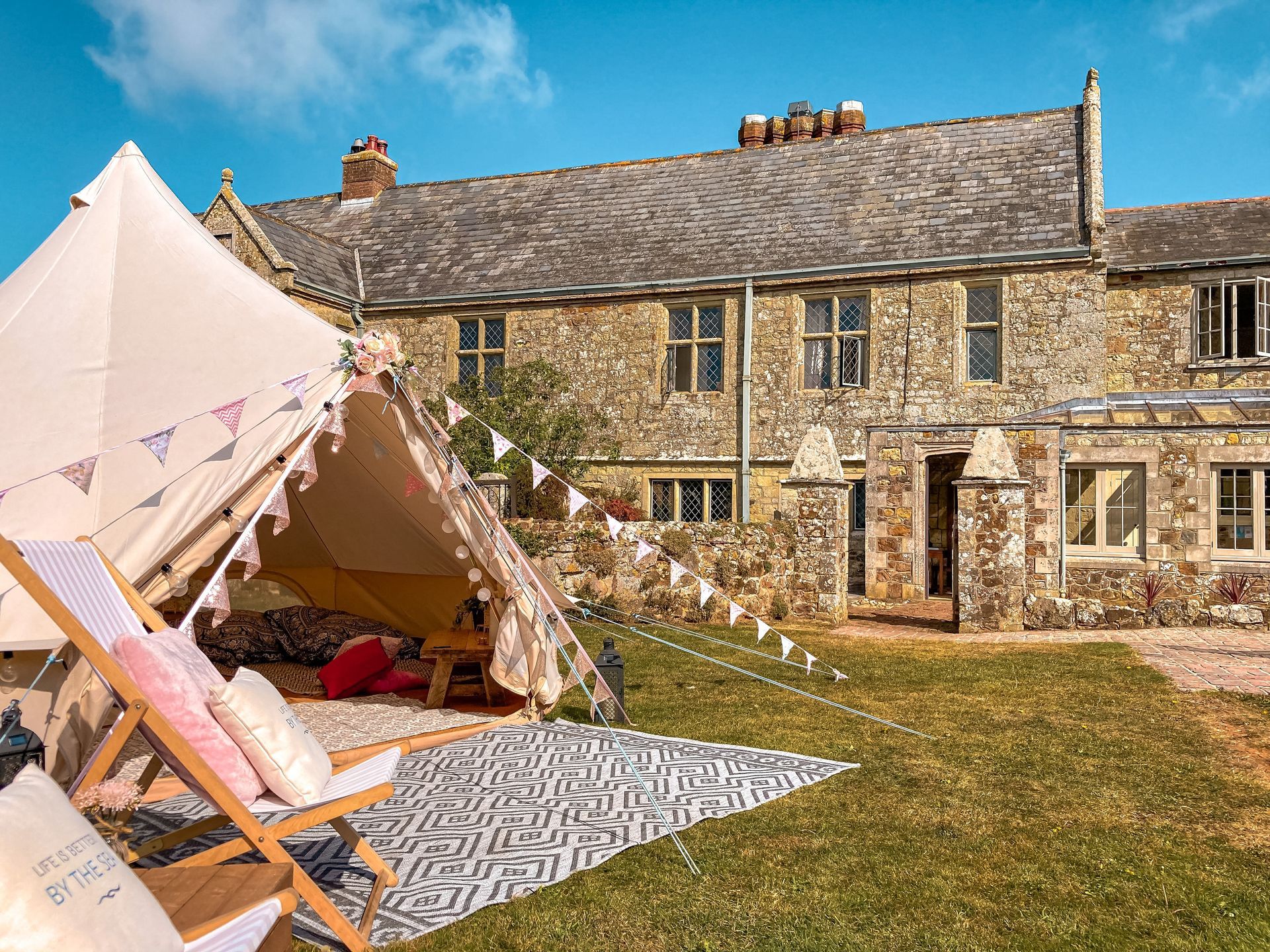 Bell tent set up in a grassy yard, with a stone building in the background and bunting.