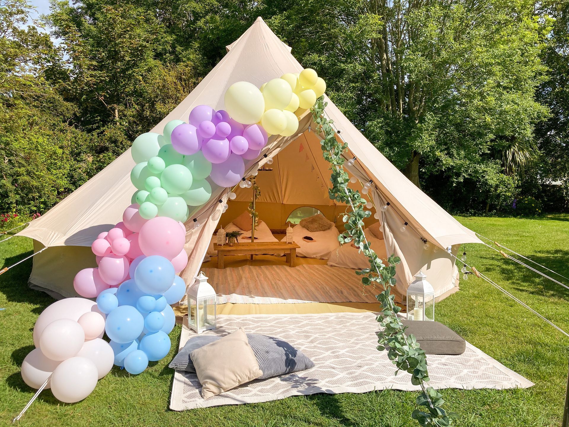 A decorated canvas tent with a pastel balloon arch in a grassy outdoor setting.