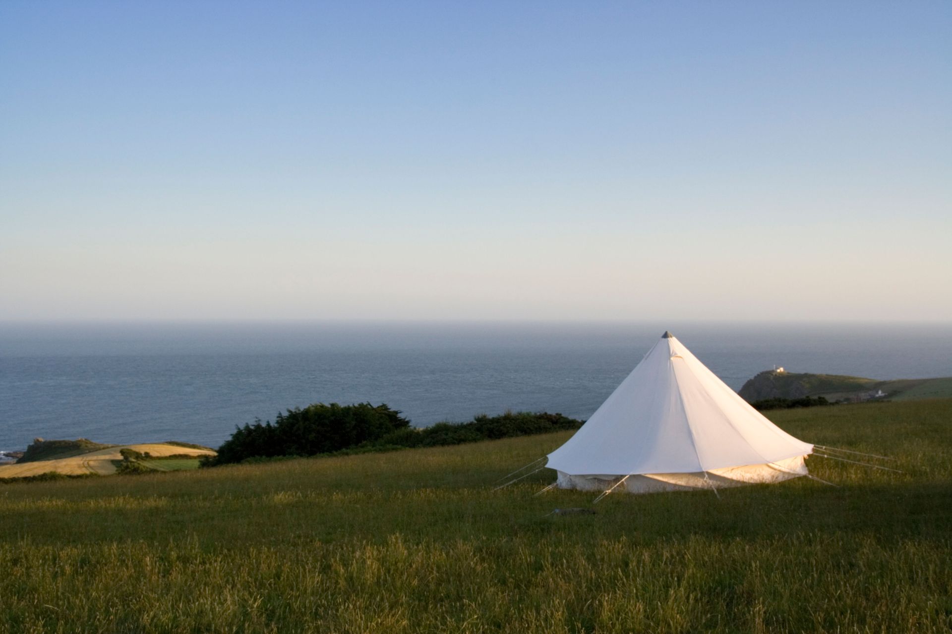 White bell tent on grassy hilltop overlooking the ocean.