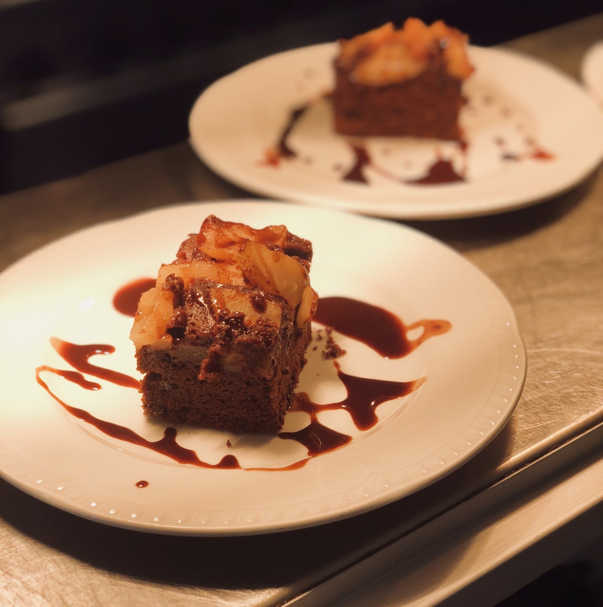 Two plates of chocolate cake topped with fruit and drizzled with chocolate sauce.