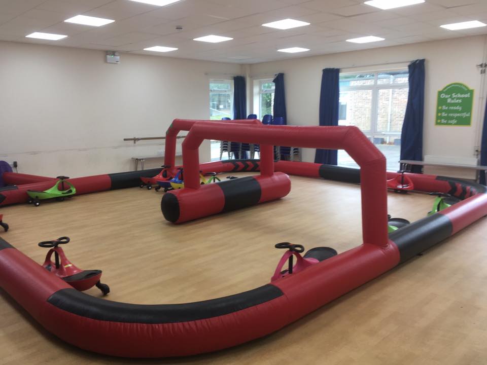 Indoor inflatable race track with toy cars, red and black, in a brightly lit room.
