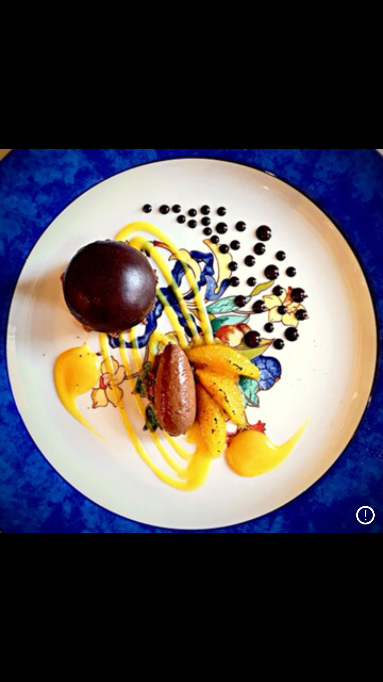 Chocolate dessert on a white plate with orange sauce, chocolate spheres, and small dots.