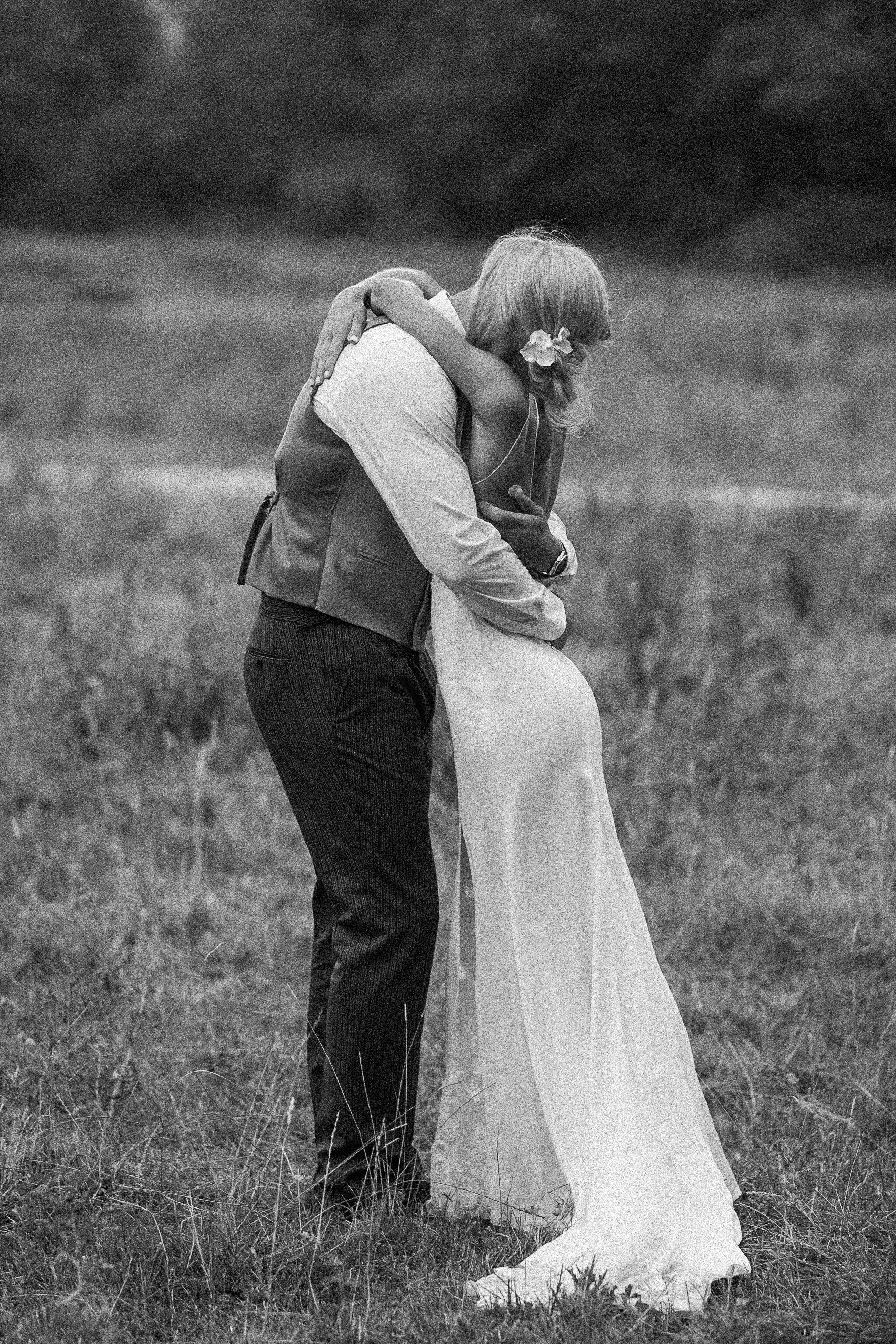 Couple embracing in a field; the woman in a white dress, the man in a vest. Black and white.