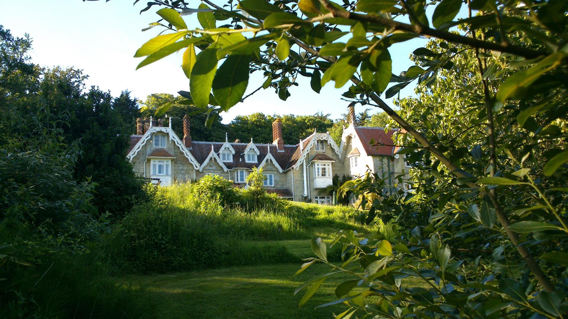 Stone house framed by lush green foliage and a grassy lawn, with blue sky peeking through.