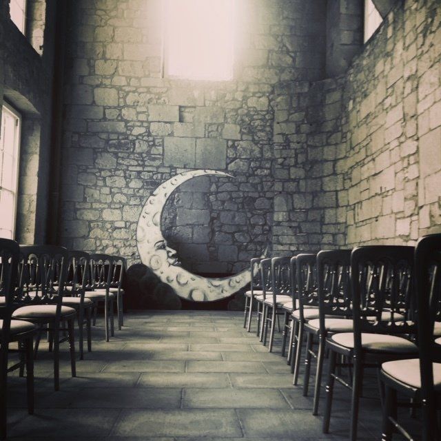 Interior with rows of chairs facing a large crescent moon painted on a stone wall.