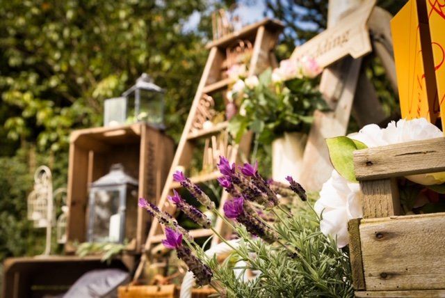 Wooden crates, ladder, and lanterns decorate an outdoor wedding setting with lavender and white flowers.