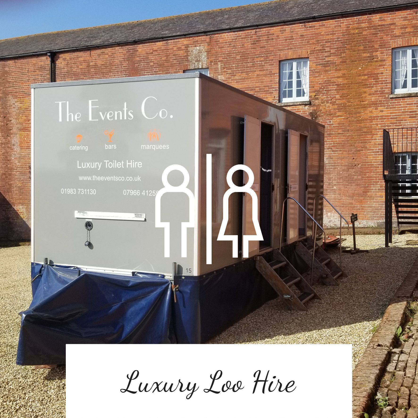 Luxury portable restroom trailer on gravel, with male/female symbols, brick building background.