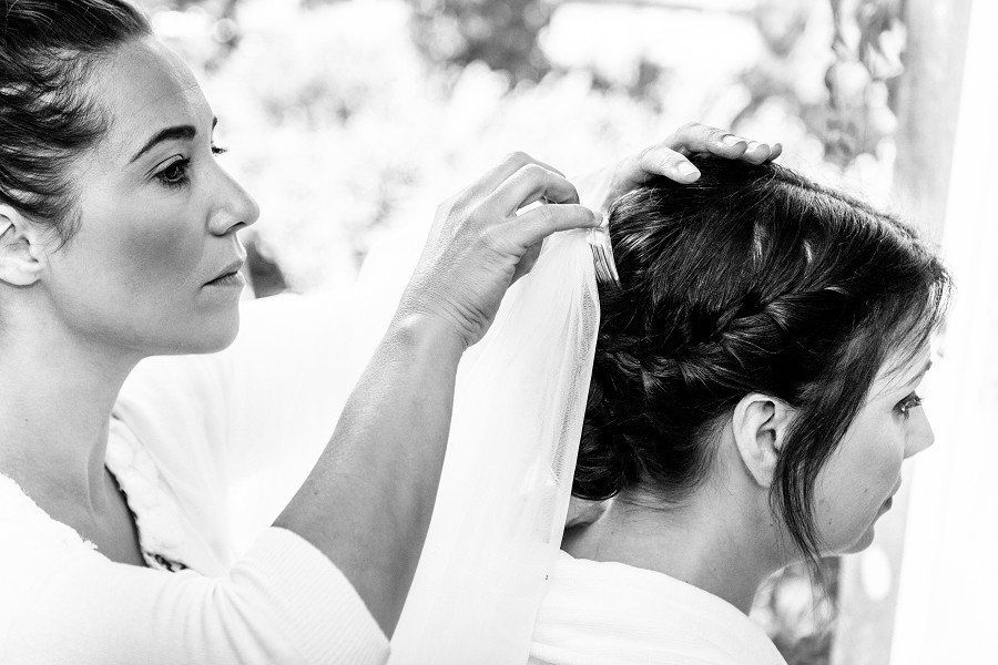 Woman styling another woman's hair in a bright setting, both wearing white.