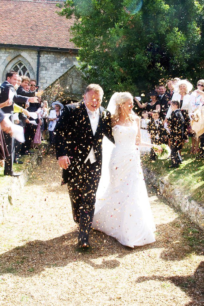 Newlyweds exiting a church, showered with confetti; the couple smiles as guests cheer.