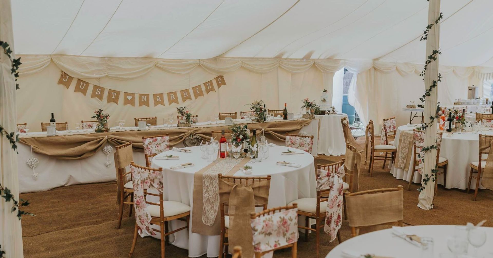 Wedding reception tent with decorated round tables and chairs, garland, and banner.