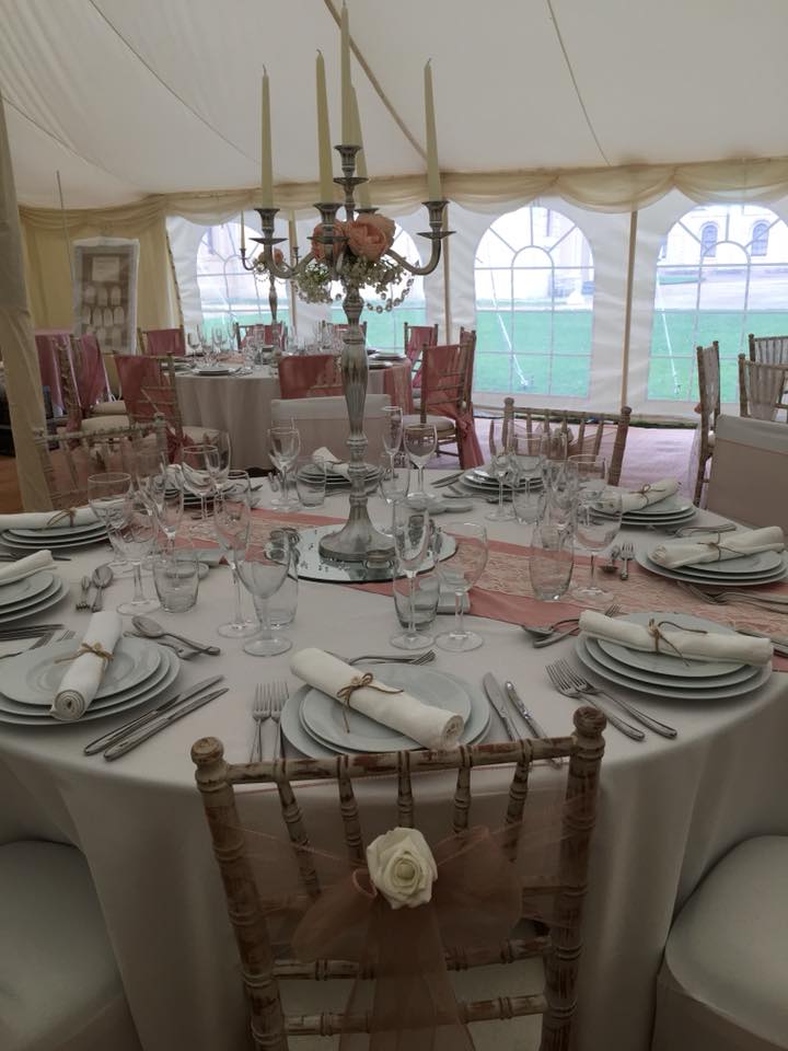 Elegant wedding reception table set in a tent, round table with place settings, centerpiece, and chairs with flower decor.