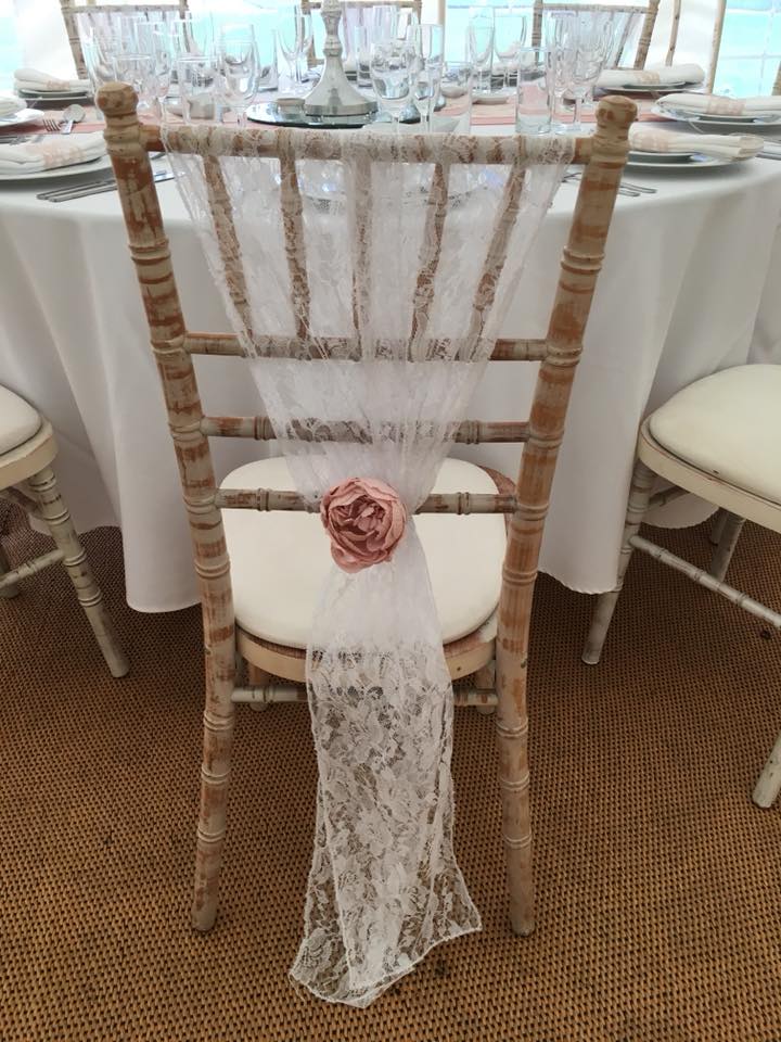A decorated wedding chair with white lace and a pink flower. Set against a white tablecloth.