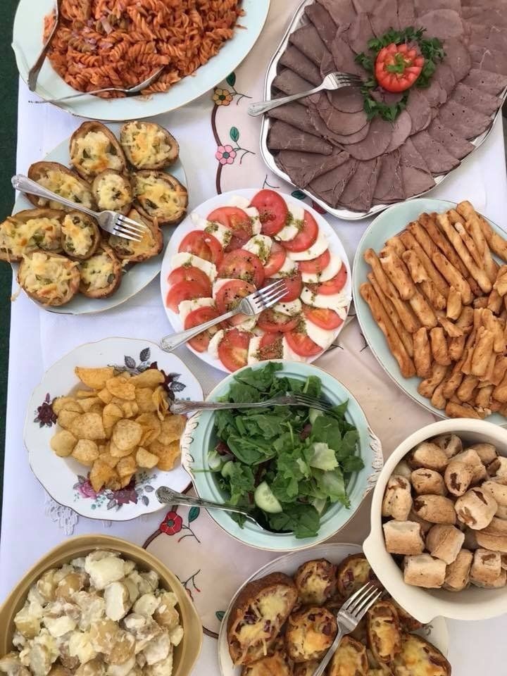 A table laden with various dishes: pasta, sliced meats, tomato-mozzarella salad, potatoes, and bread.