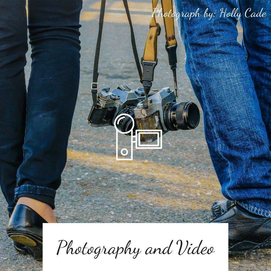 Two people walking, holding a camera between them. One wears black pants, the other jeans.