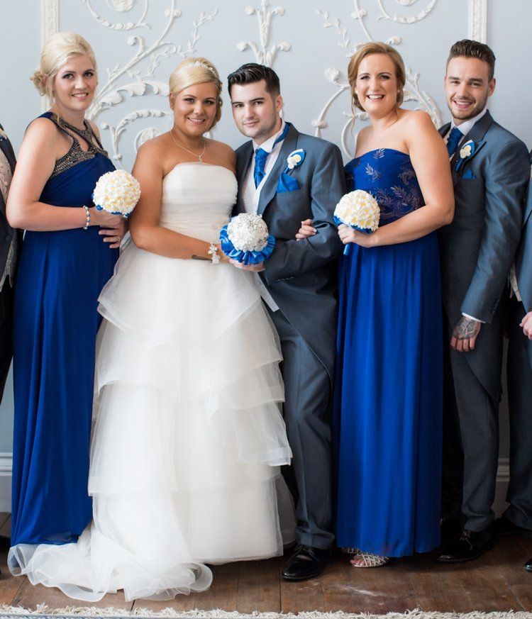 Wedding party poses: bride in white gown with attendants in blue dresses and groom in grey suit.
