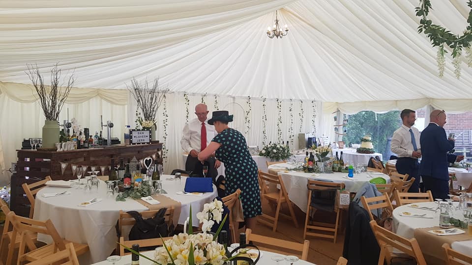 Wedding reception tent with decorated tables, guests mingling, and a couple in the center.