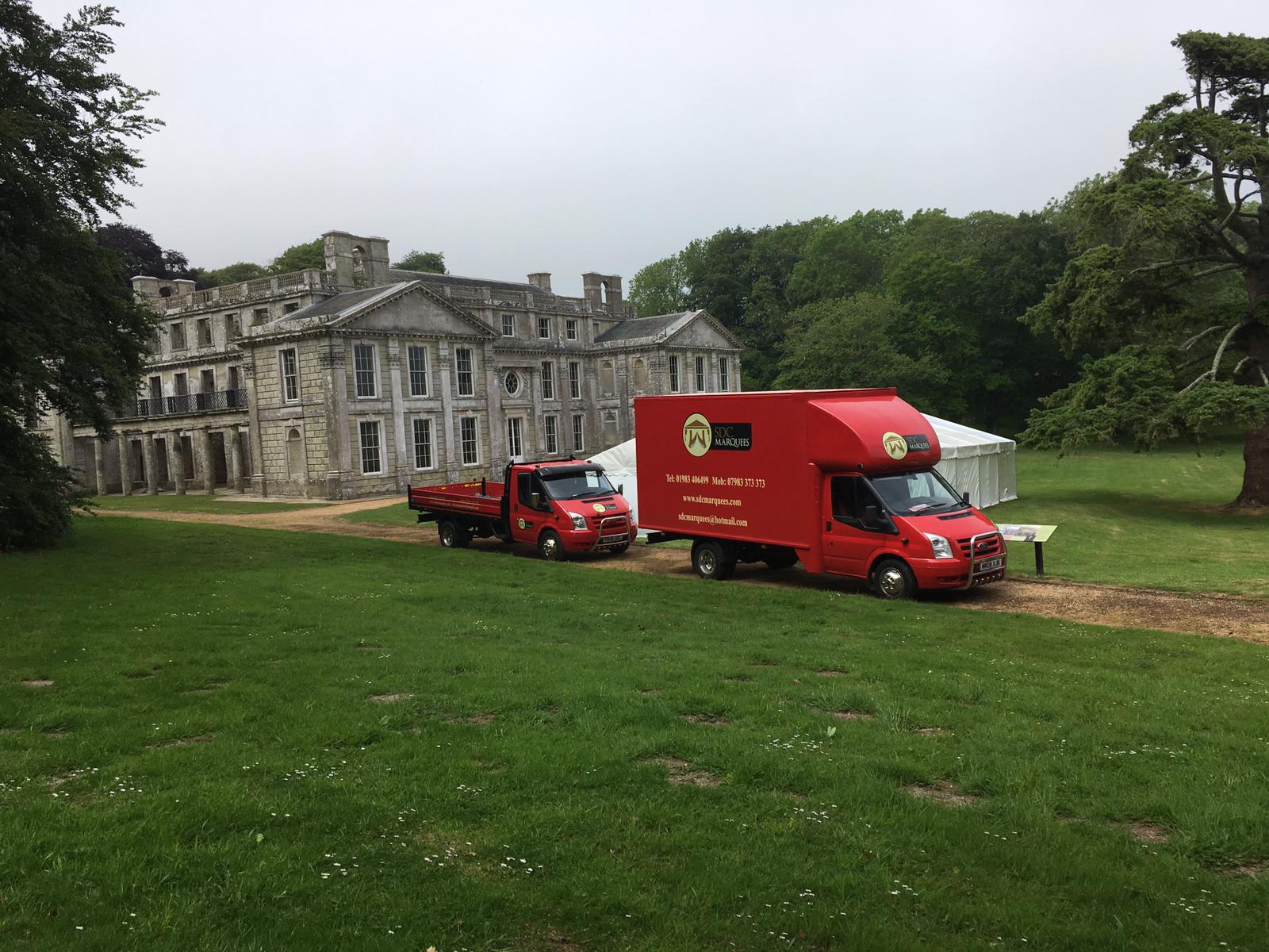 Two red trucks in front of a weathered stone mansion on a grassy lawn.