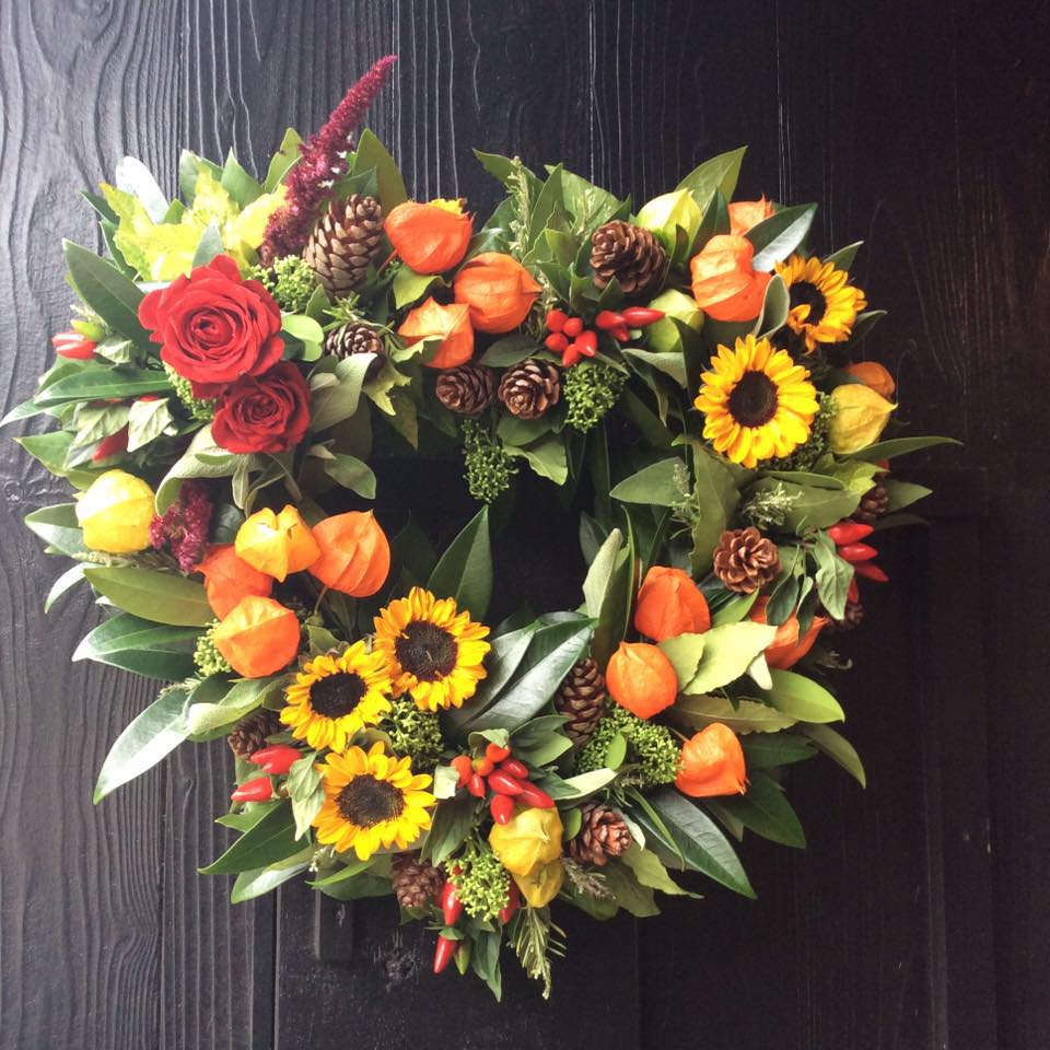 Colorful autumnal wreath with roses, sunflowers, and orange lantern flowers, on a dark door.