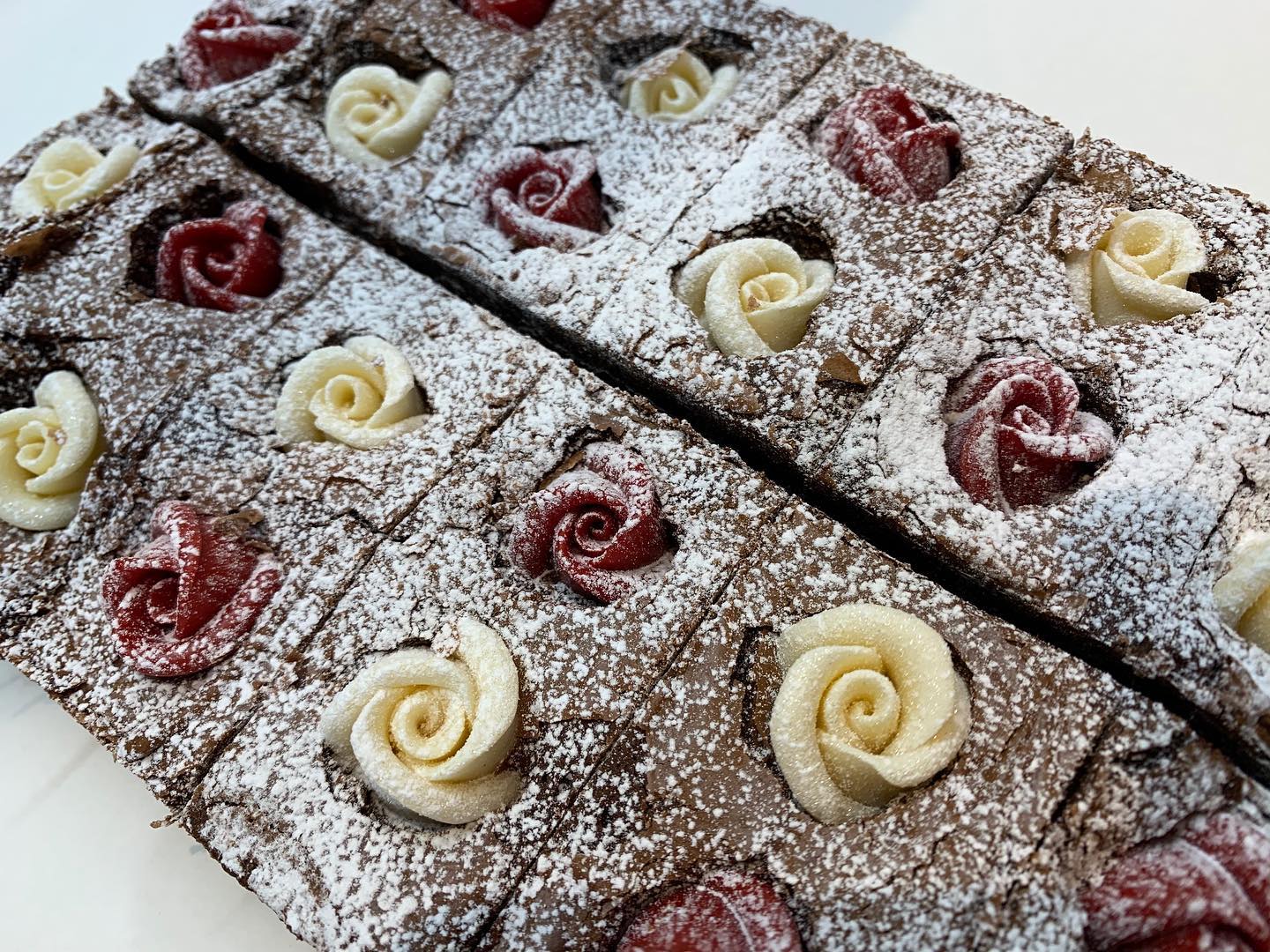 Brownie squares with white and red frosting rose decorations, dusted with powdered sugar.