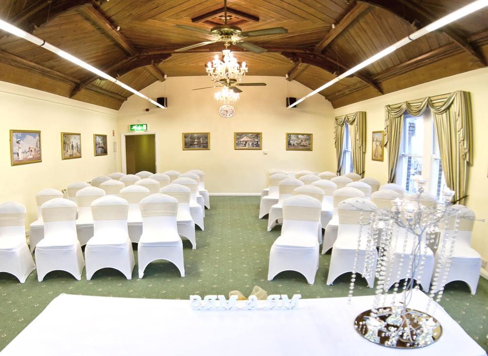 An empty wedding ceremony room with white chairs, a table, and a chandelier.