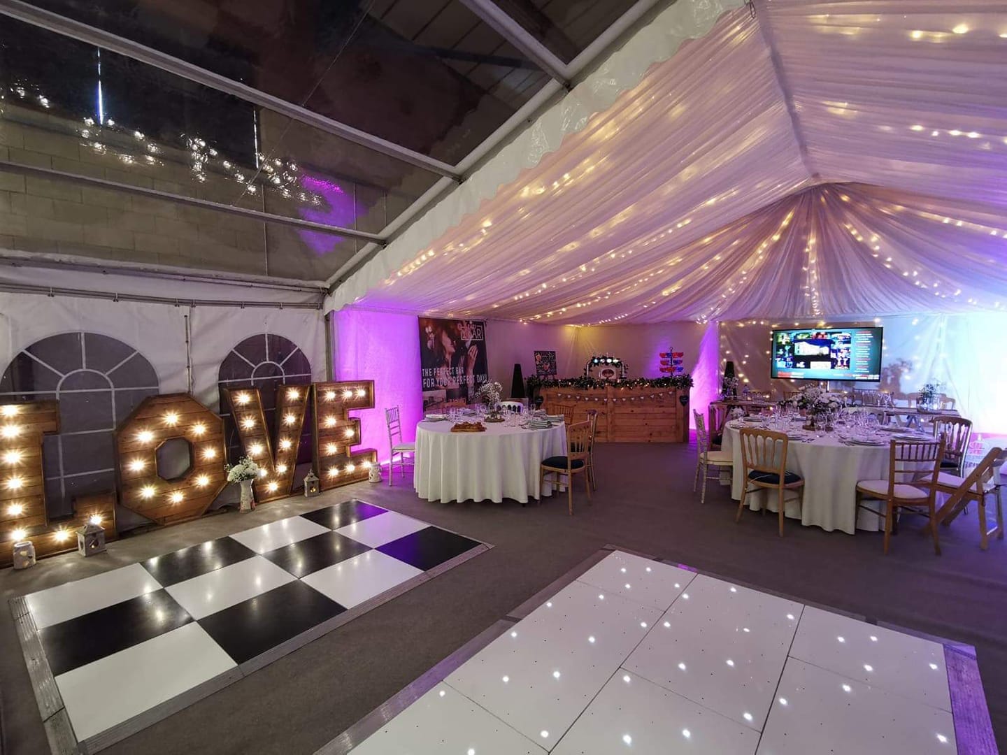Wedding reception tent with dance floors, tables, string lights, and LOVE letters.