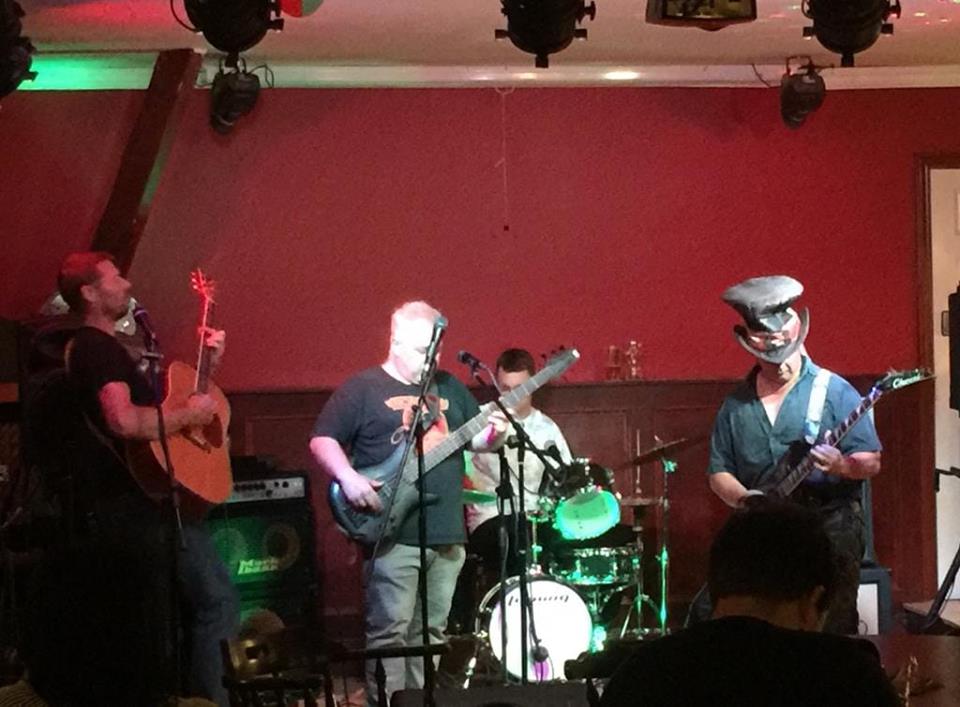 Band playing on stage with red background and stage lighting.