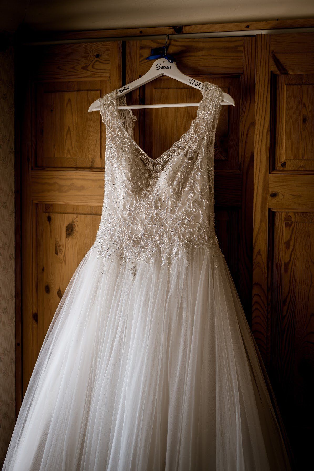 Wedding dress hanging on a wooden wardrobe. The dress is white with beaded bodice and tulle skirt.