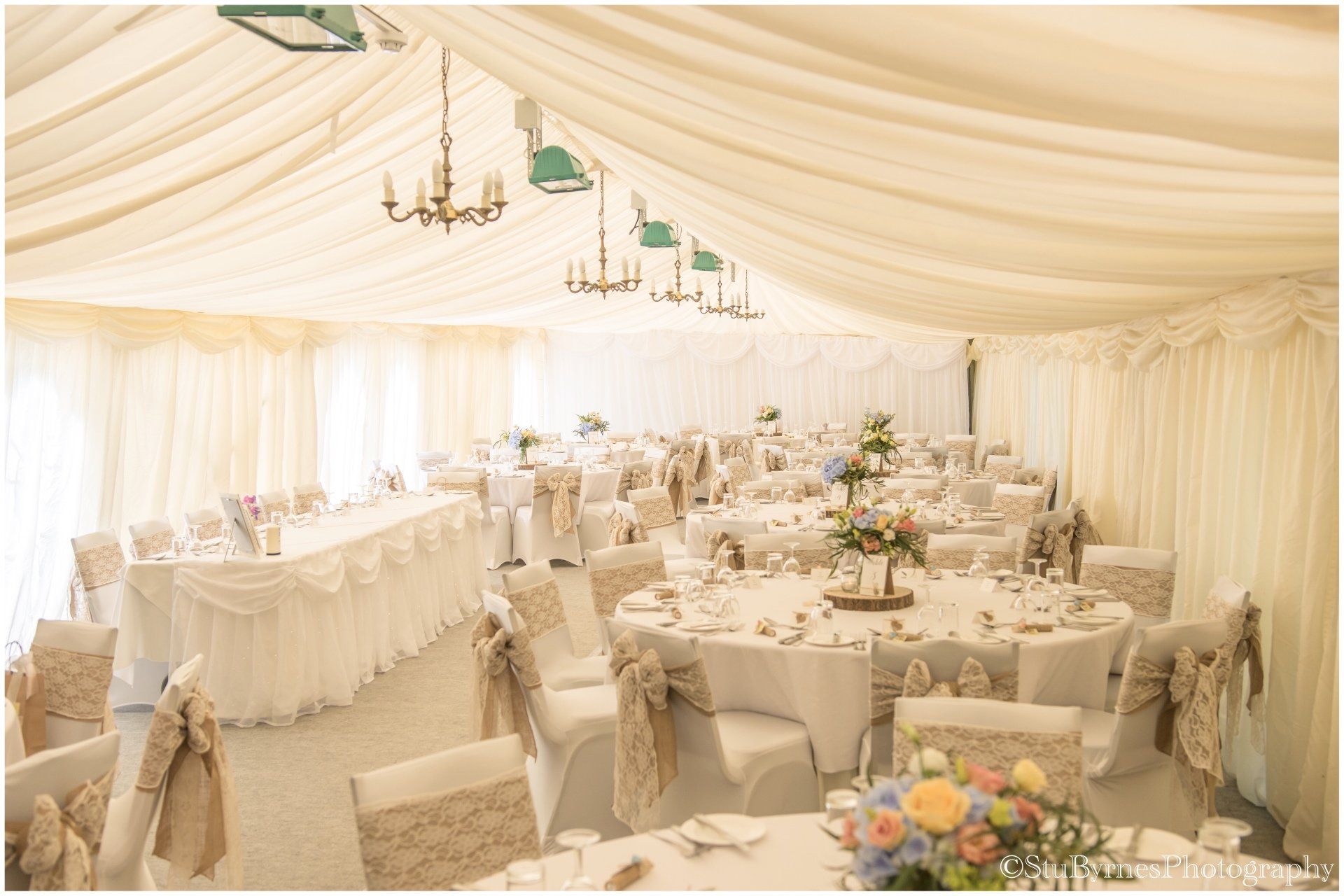 Elegant wedding reception inside a white tent, round tables with centerpieces, chairs with covers.
