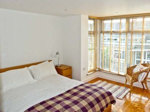 Bedroom with bed, bedside table, armchair by window with blinds, wooden floor.