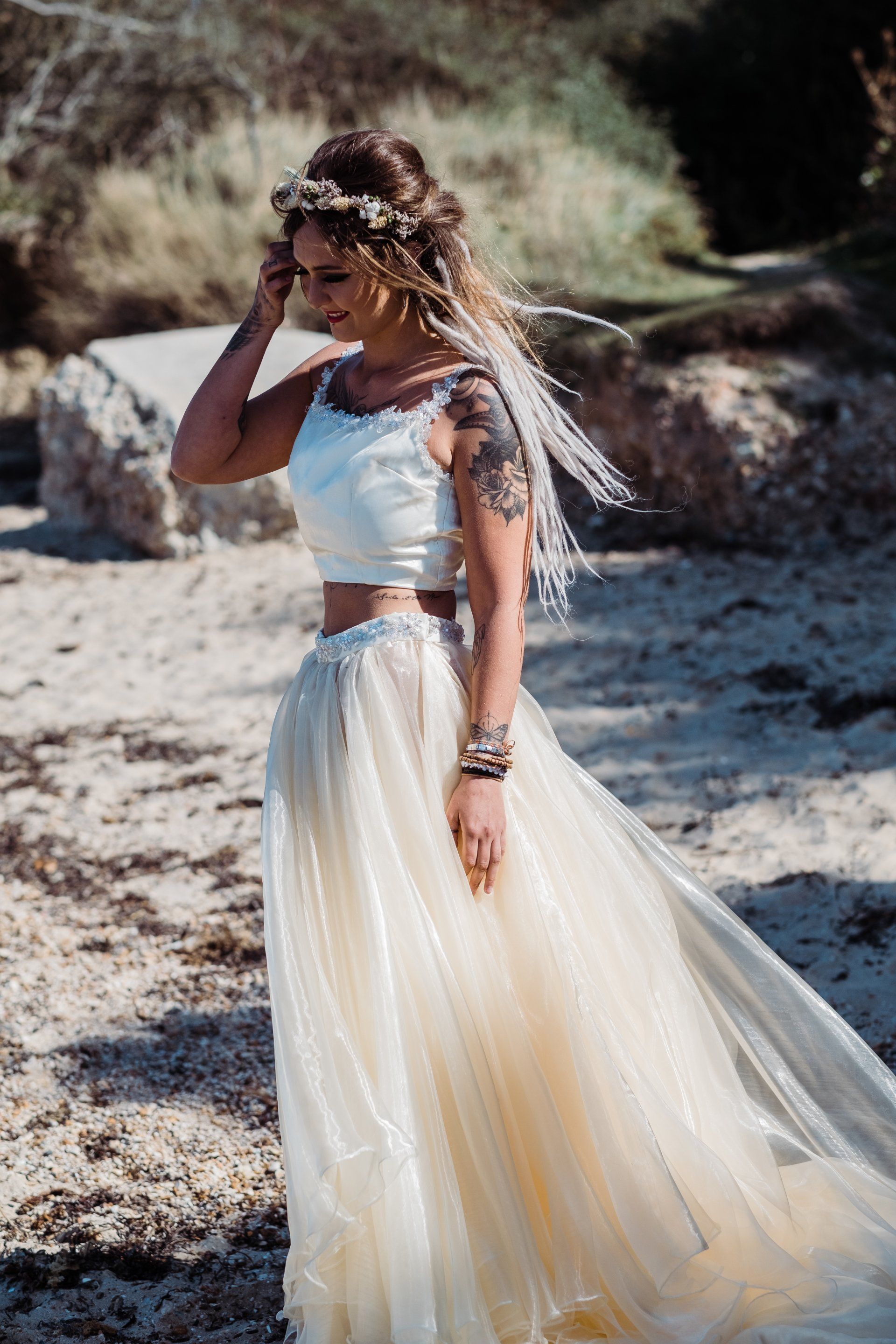 Woman in crop top and tulle skirt, wearing floral crown, on a beach.
