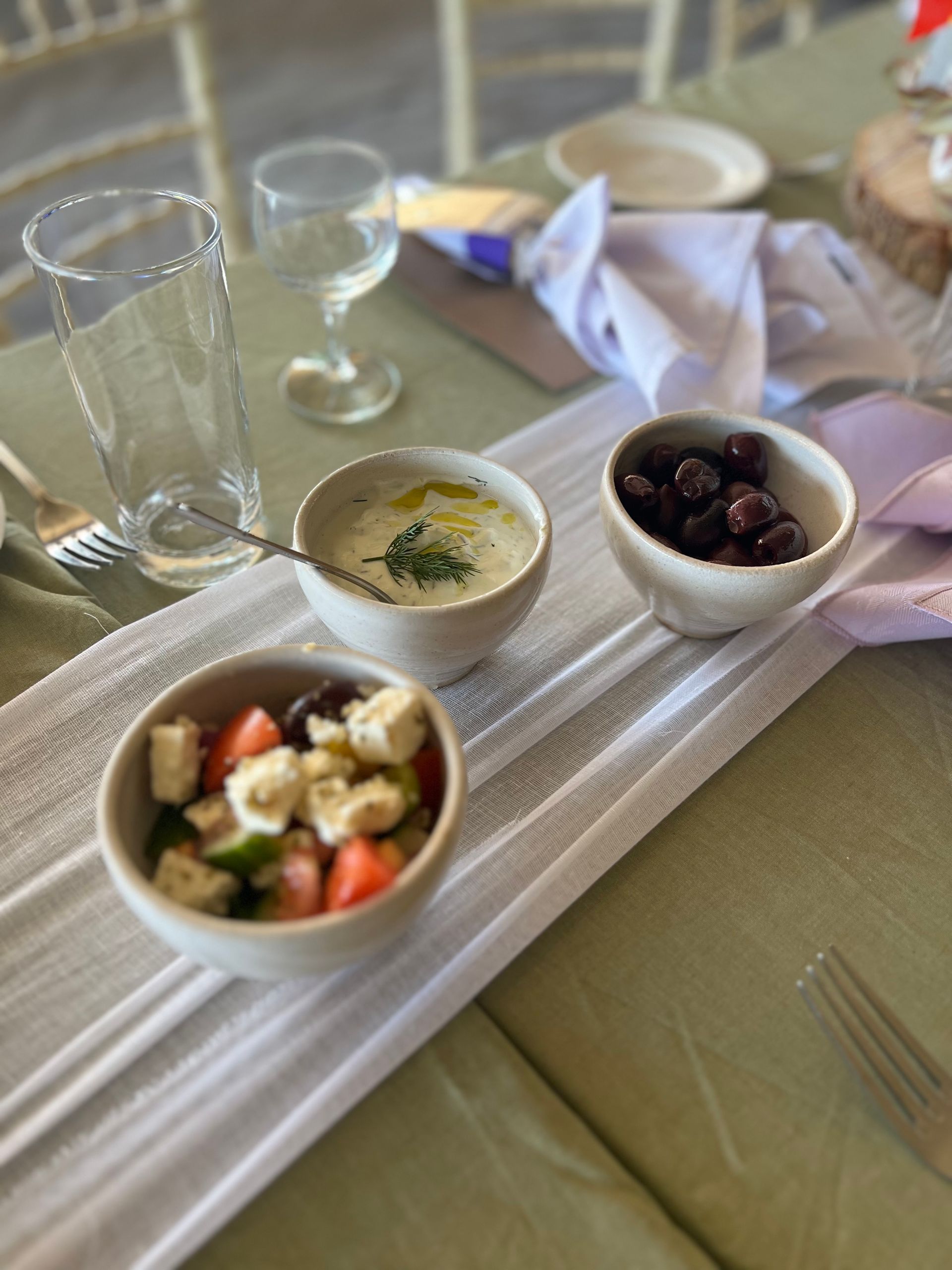 Table setting with three small bowls: Greek salad, tzatziki, and olives.