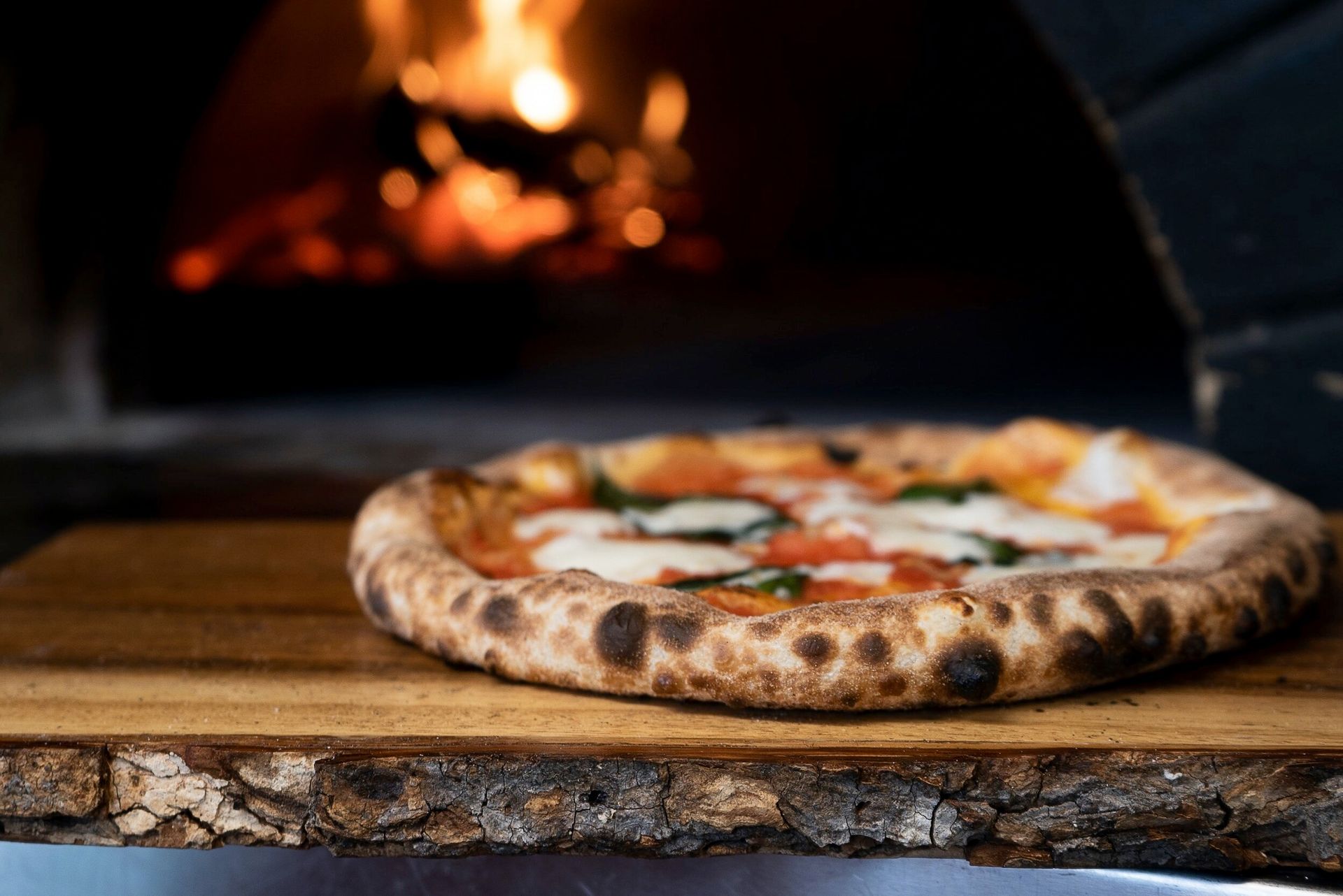 Pizza on wooden board in front of a wood-fired oven.