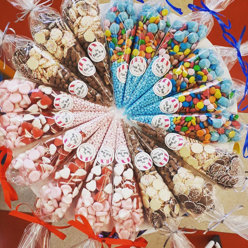 Arrangement of assorted candy-filled cellophane cones, tied with ribbons, displayed on a table.