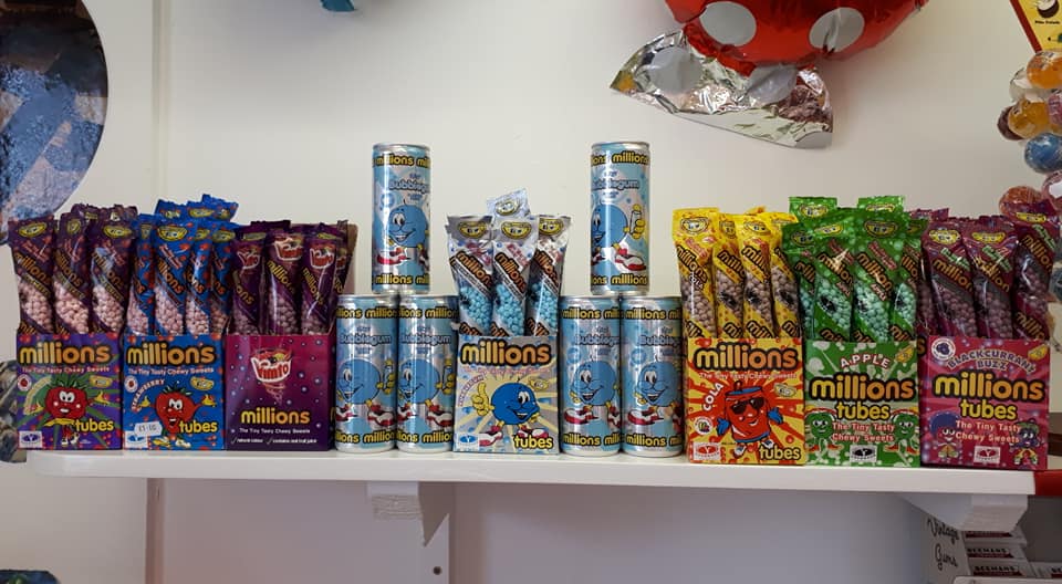 Display of colorful Millions candies on a shelf, including tubs and bags with various flavors.