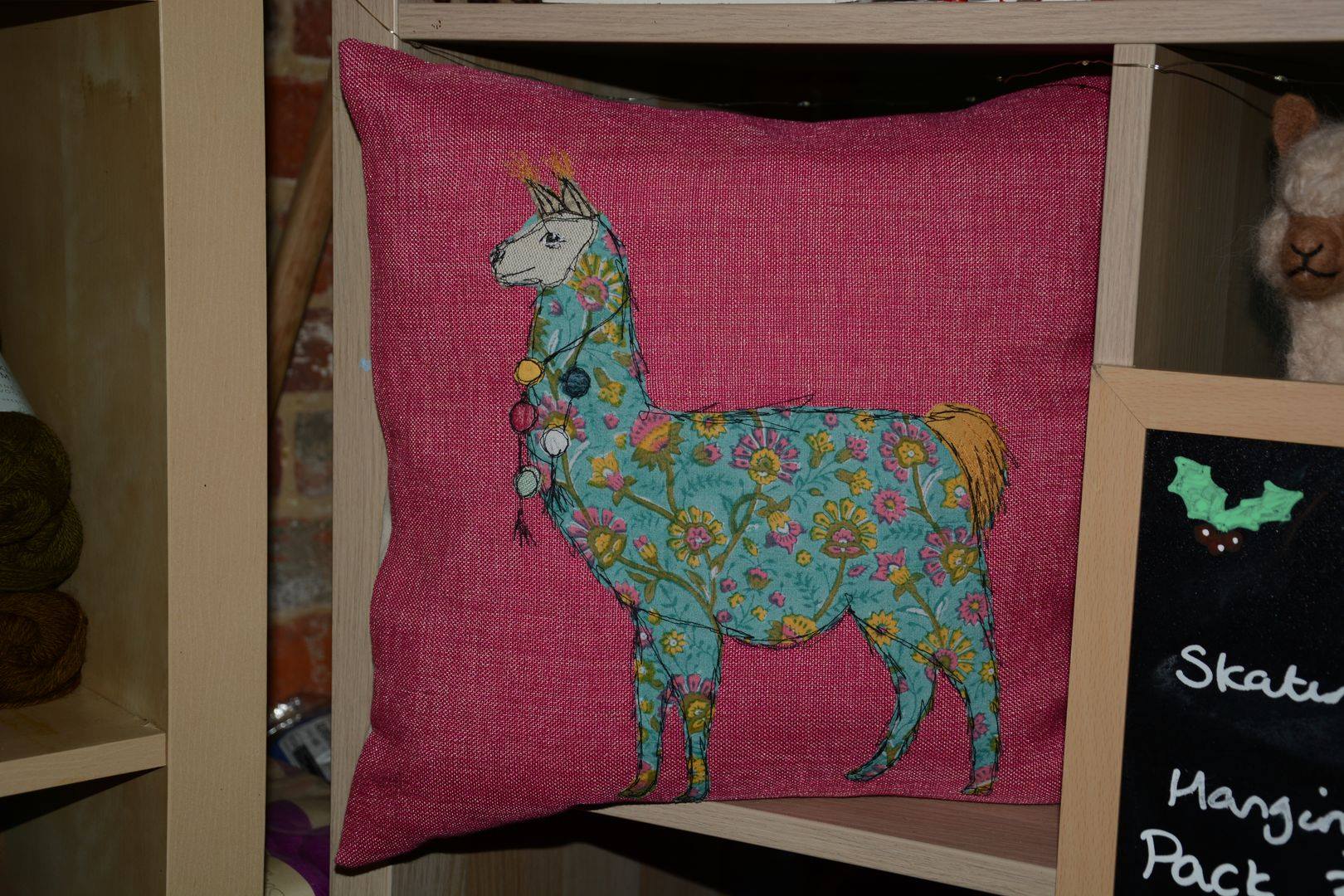 Llama pillow with floral pattern on a pink background, displayed on a shelf.