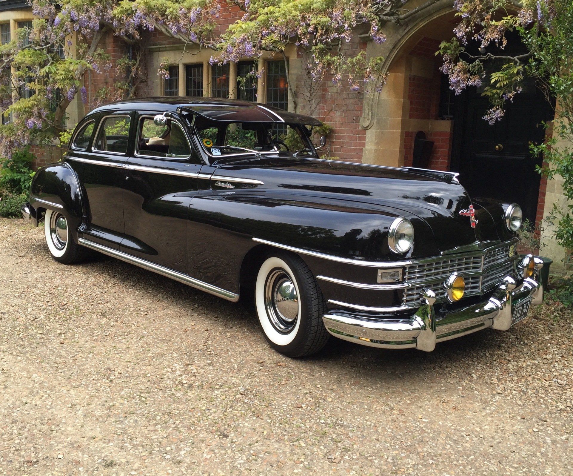Black vintage Chrysler car parked in front of a stone building with a gravel driveway.
