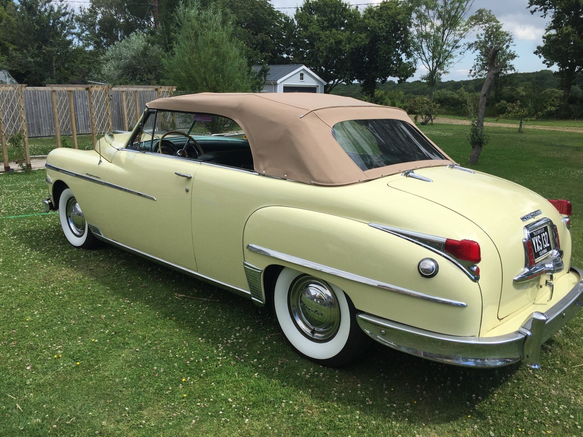 Light yellow convertible car with a tan roof parked on grass.