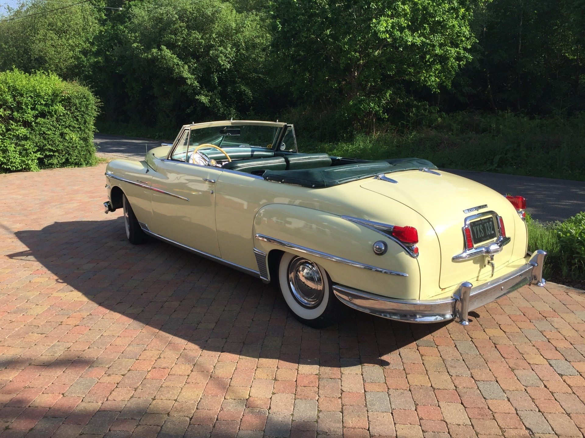 Yellow vintage convertible car parked on a brick driveway, top down. Green interior.