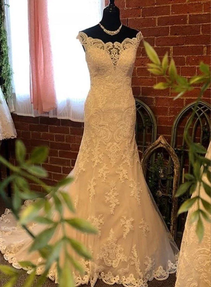 Wedding gown on a mannequin, off-the-shoulder neckline, lace overlay, displayed in a bridal shop.