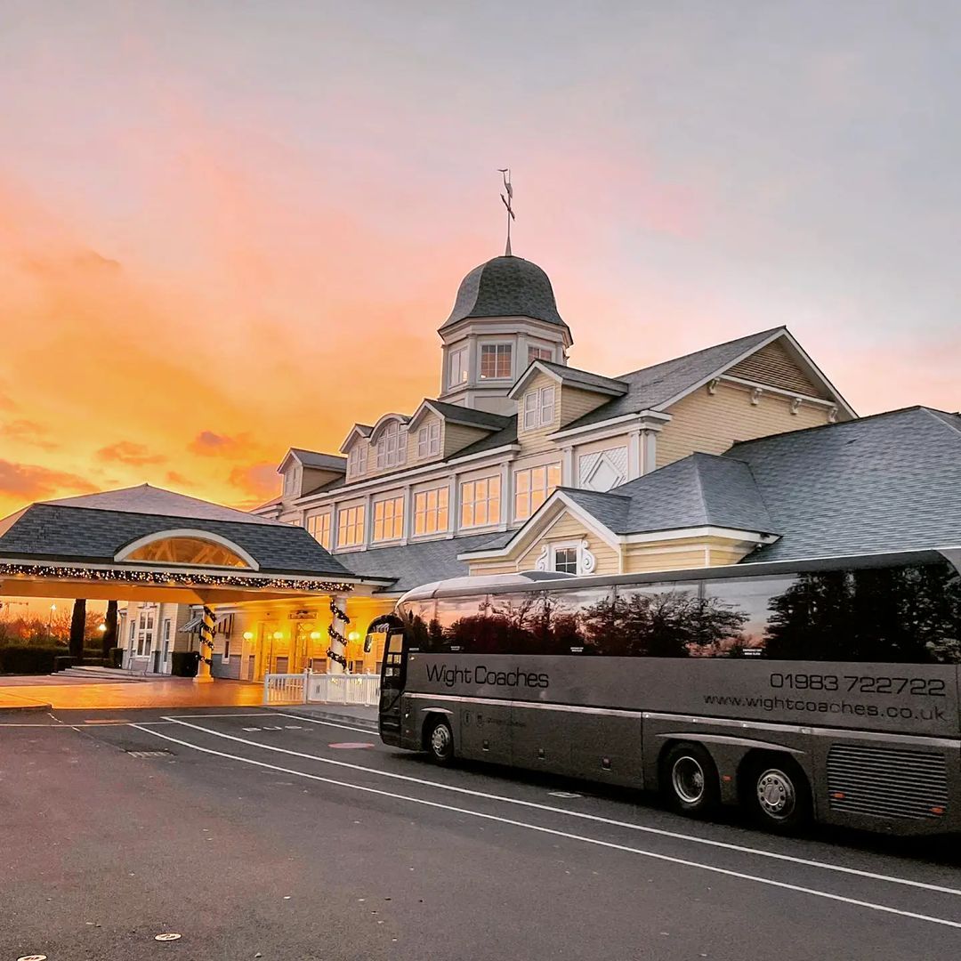 Bus parked in front of a large, ornate building at sunset. Yellow and orange sky.