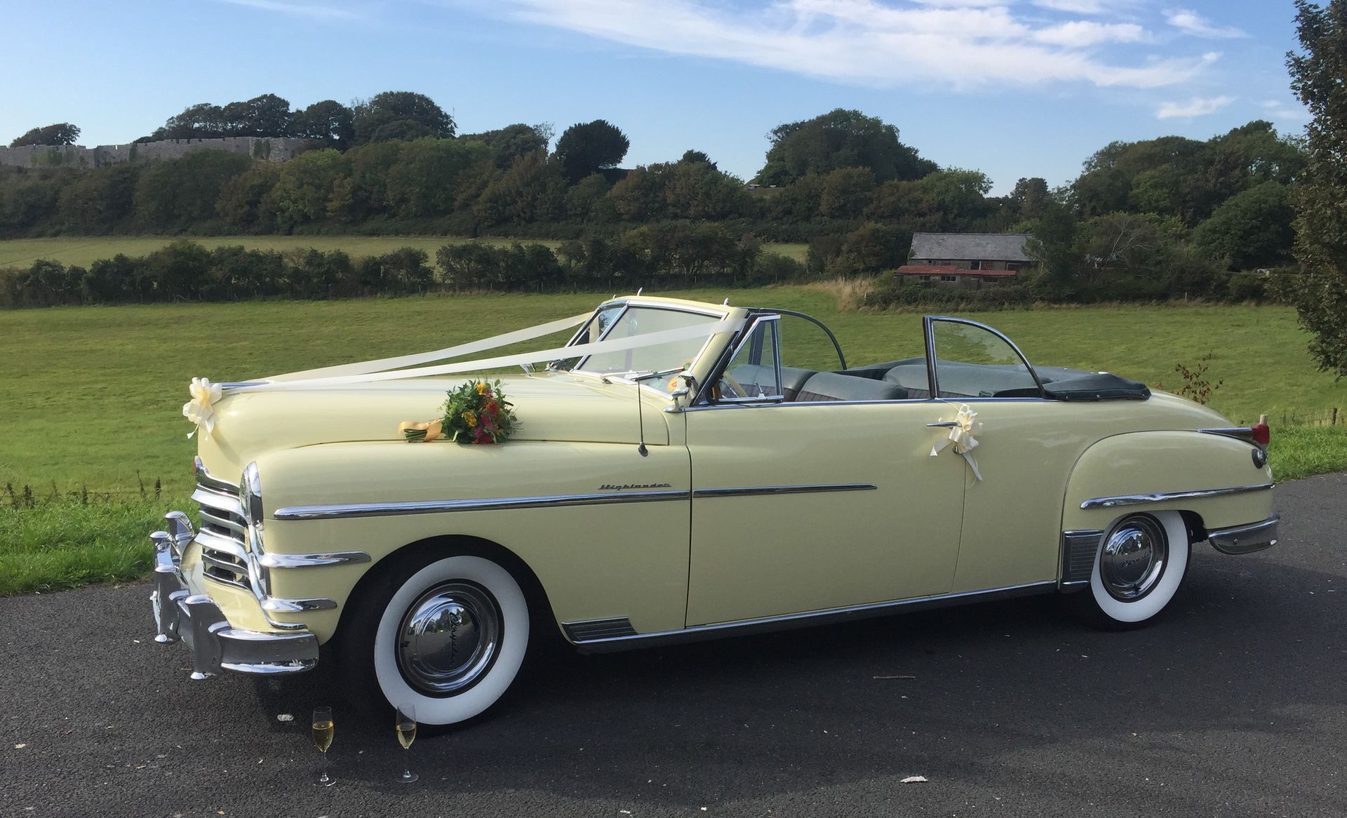 Yellow vintage convertible car decorated with wedding ribbons, parked outdoors on a sunny day.