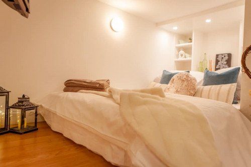 Cozy bedroom with a bed, pillows, and decorative lanterns. White walls and wooden floor.