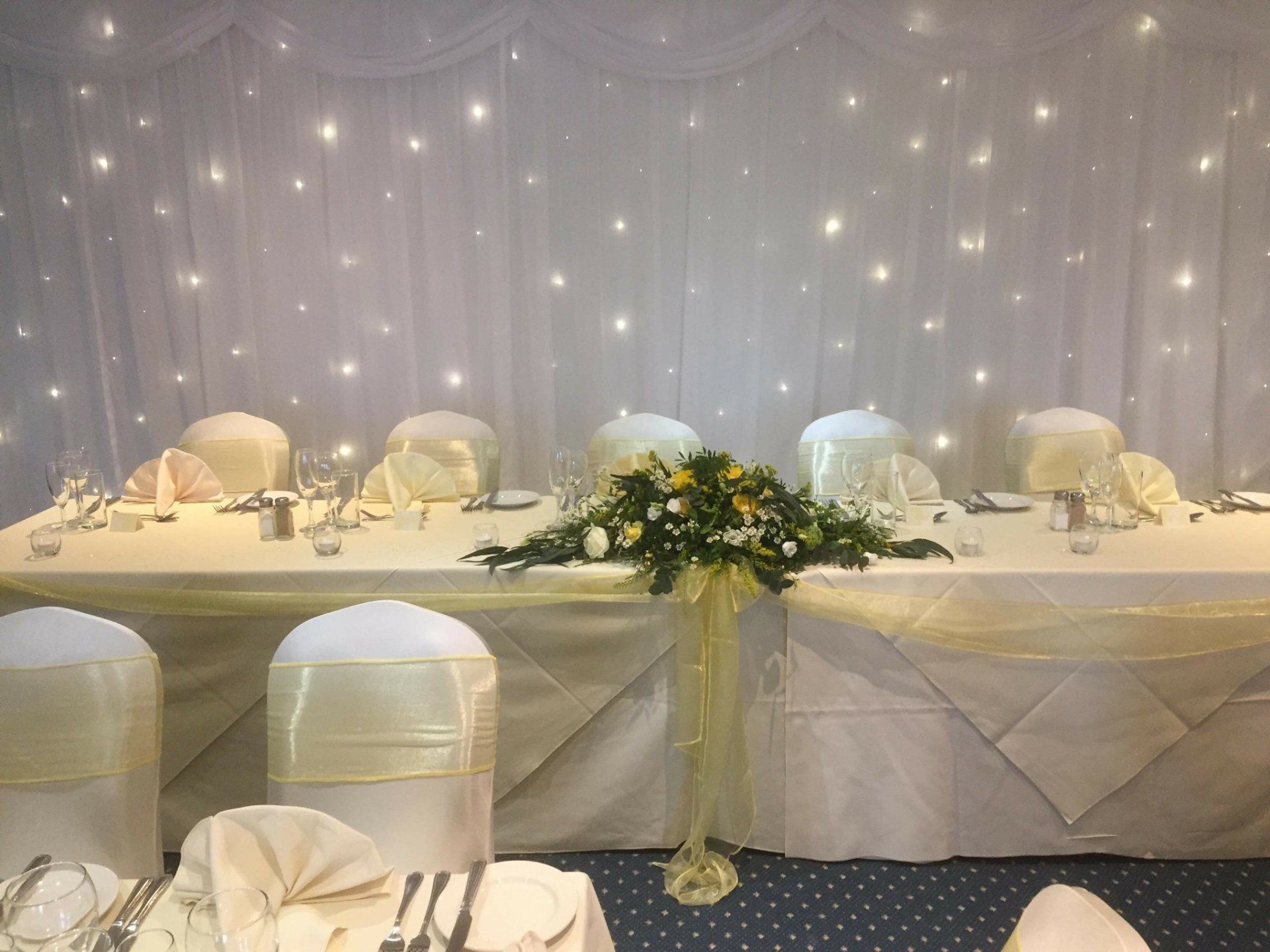 Wedding reception table with floral centerpiece, cream-colored decor, and a twinkling star backdrop.