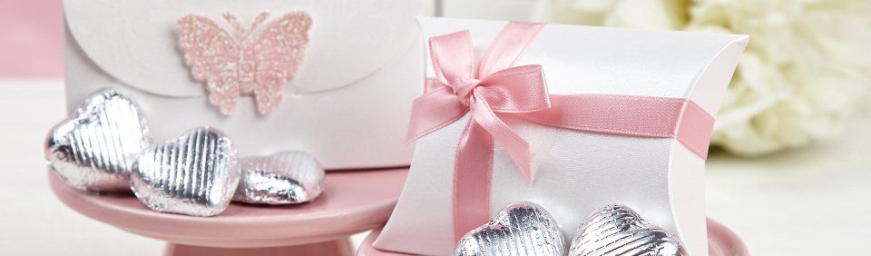 White gift boxes with pink ribbon and butterfly, heart-shaped candies on a pink cake stand.